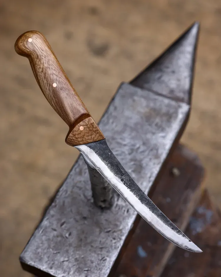 A long bladed knife with a wooden handle resting on an anvil.